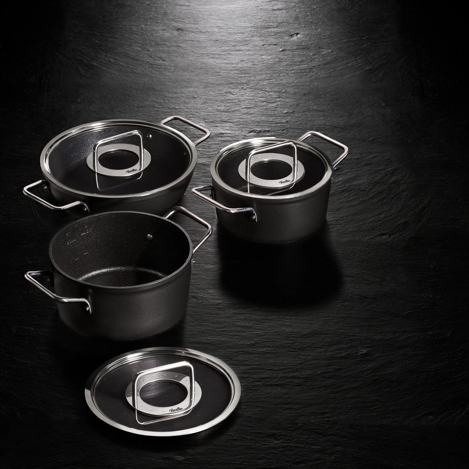 Set of black cookware with glass lids on a dark surface
