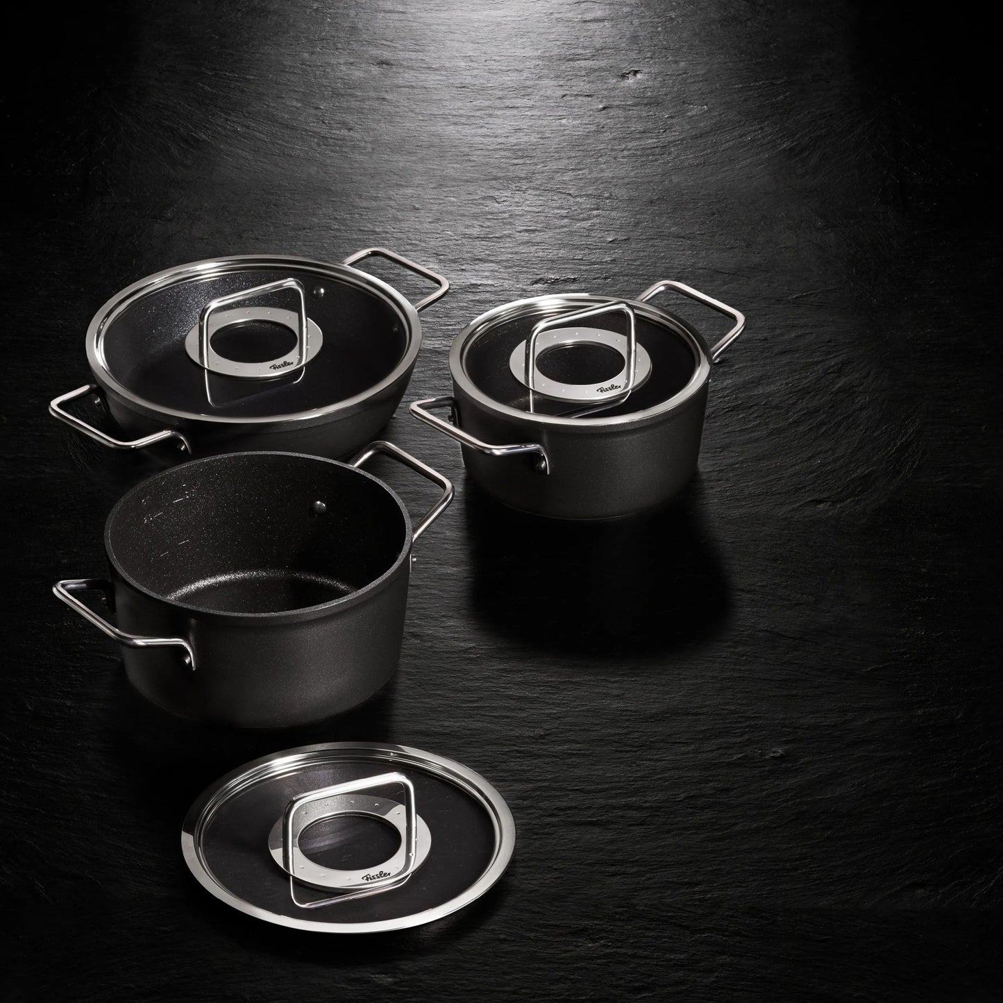 Set of black cookware with glass lids on a dark surface