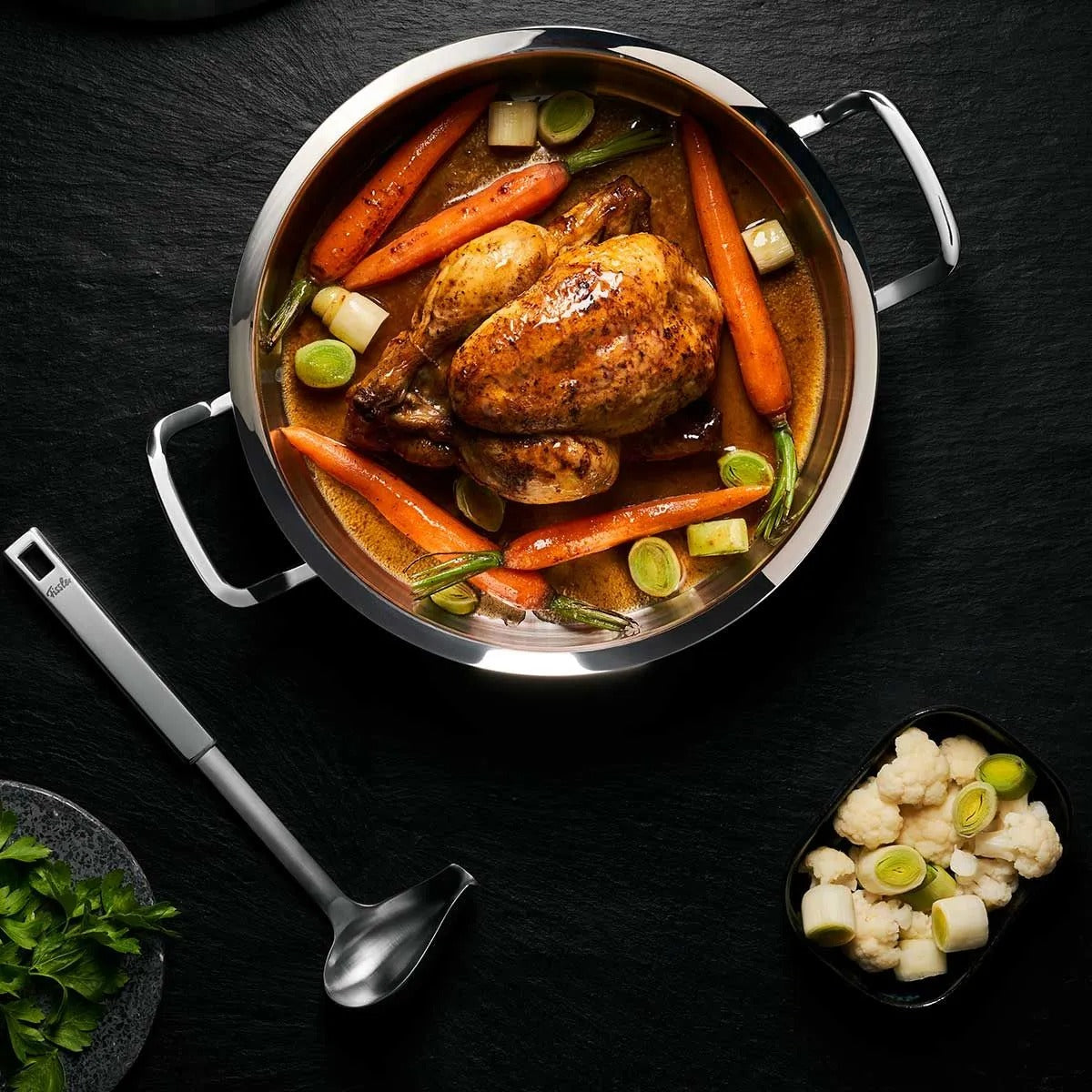 Roasted chicken with carrots and onions in a pot on a dark surface
