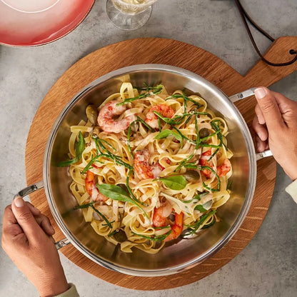 Stir-fried pasta with shrimp and greens in a metal pan on a wooden board.